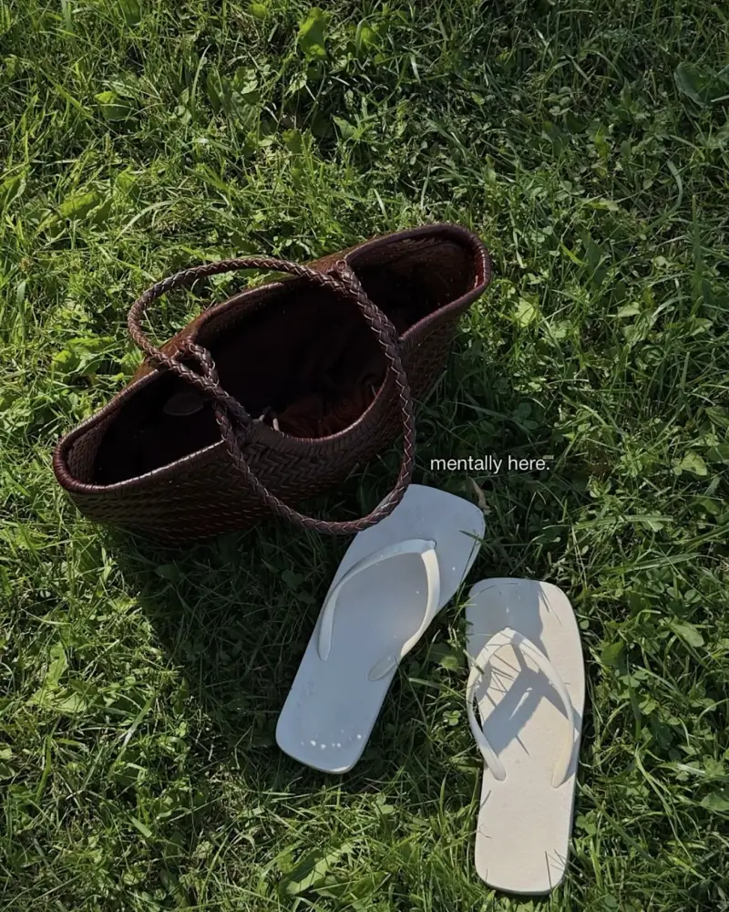 Woven leather tote and white flip-flops on the grass, captioned mentally here.