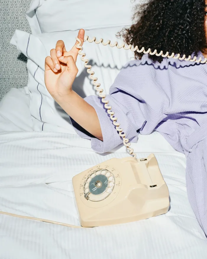 A hand twisting a phone cord in bed, lavender robe sleeve